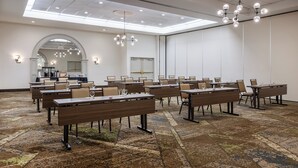 Un salón de conferencias con varias mesas y sillas, una alfombra estampada y un candelabro moderno.