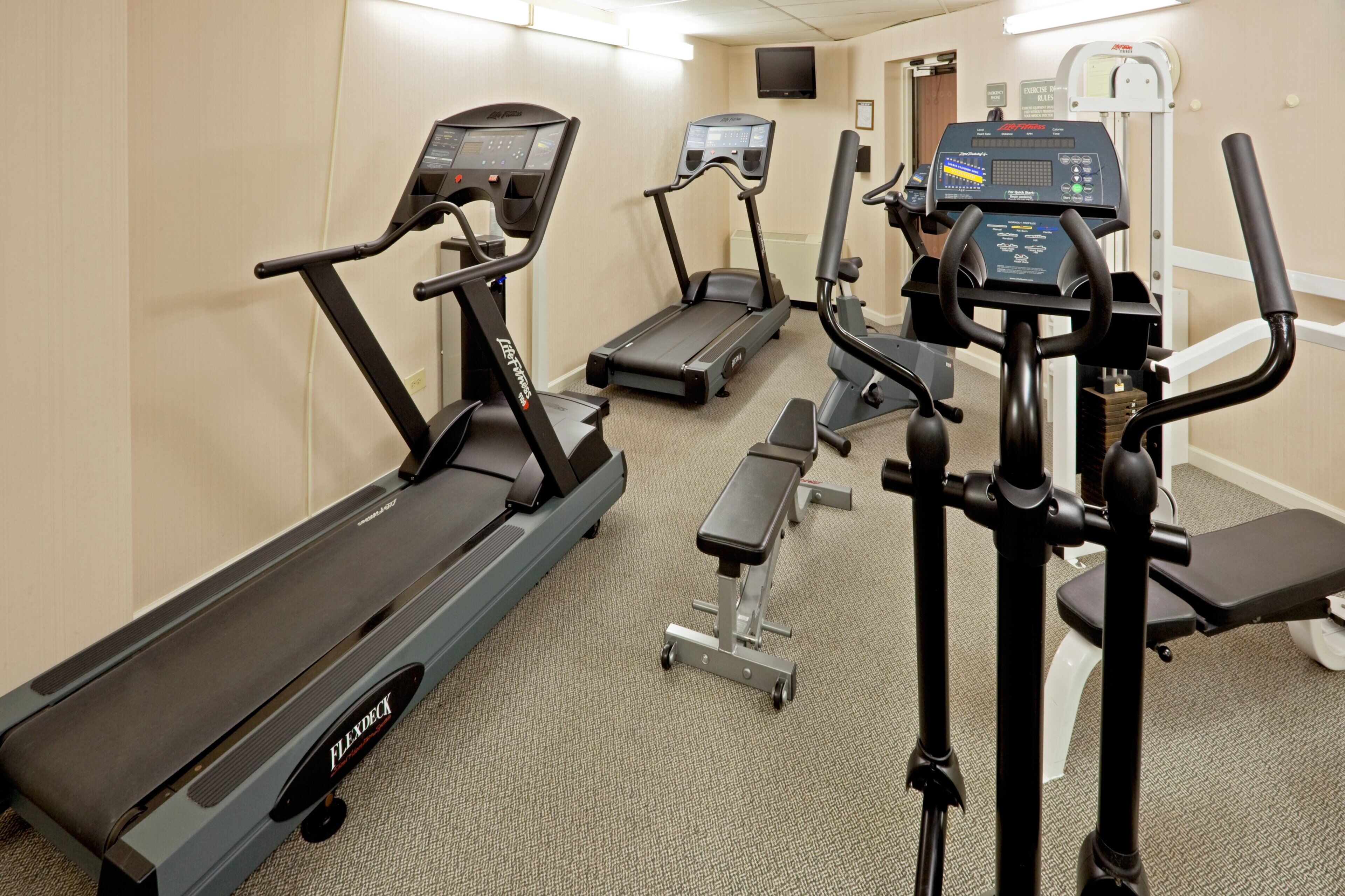 A hotel fitness center with treadmills, a stationary bike, and a weight bench.