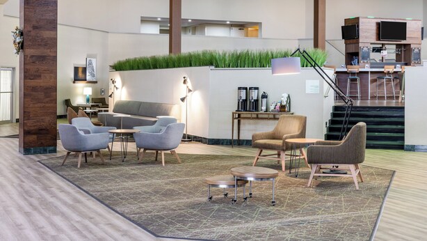Un vestíbulo moderno con áreas de descanso, una estación de café y una escalera que conduce a los pisos superiores.