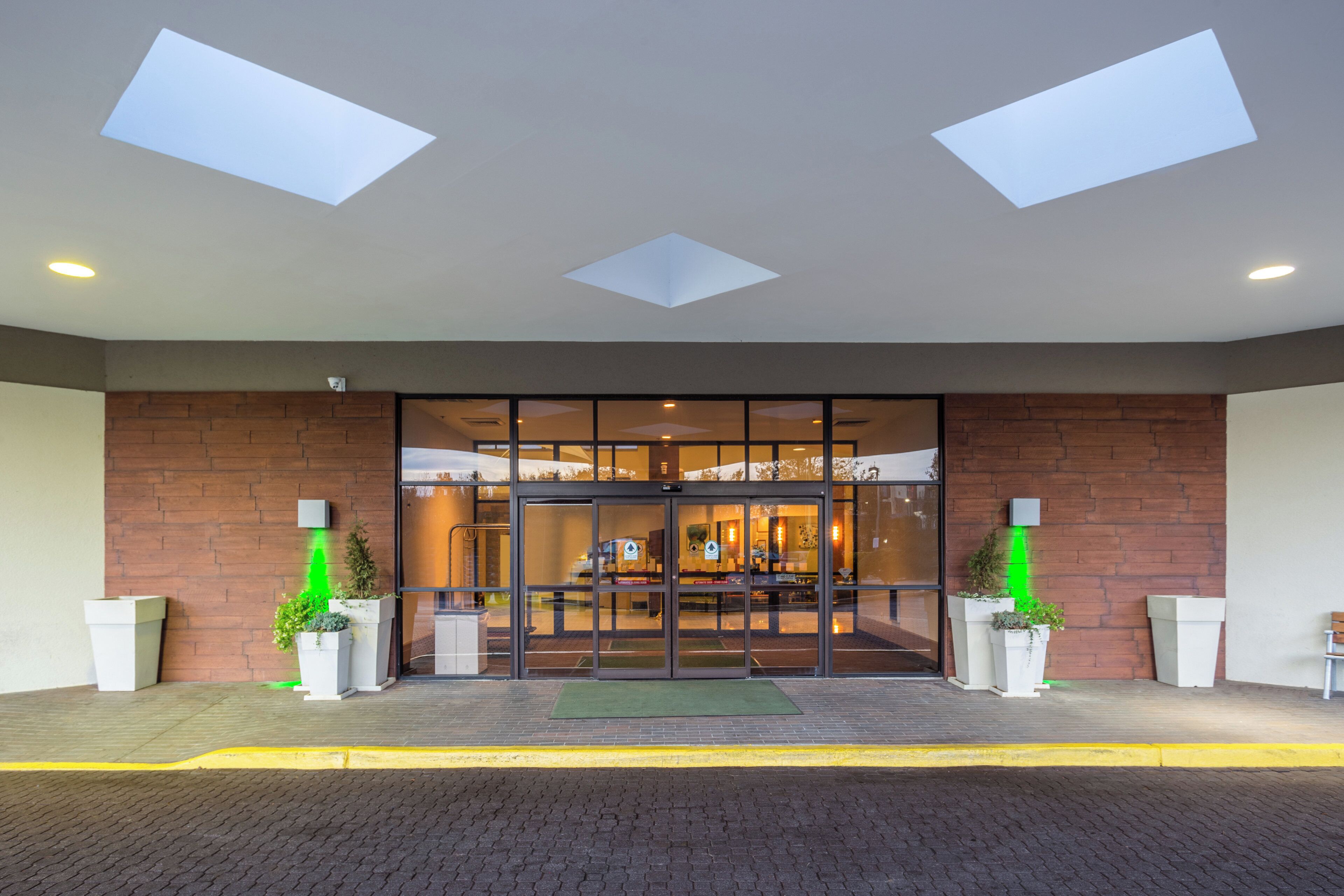 A hotel entrance with a brick facade, large glass doors, and a green mat at the entrance.