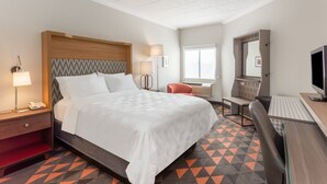 A hotel room with a bed, desk, chair, and a TV.