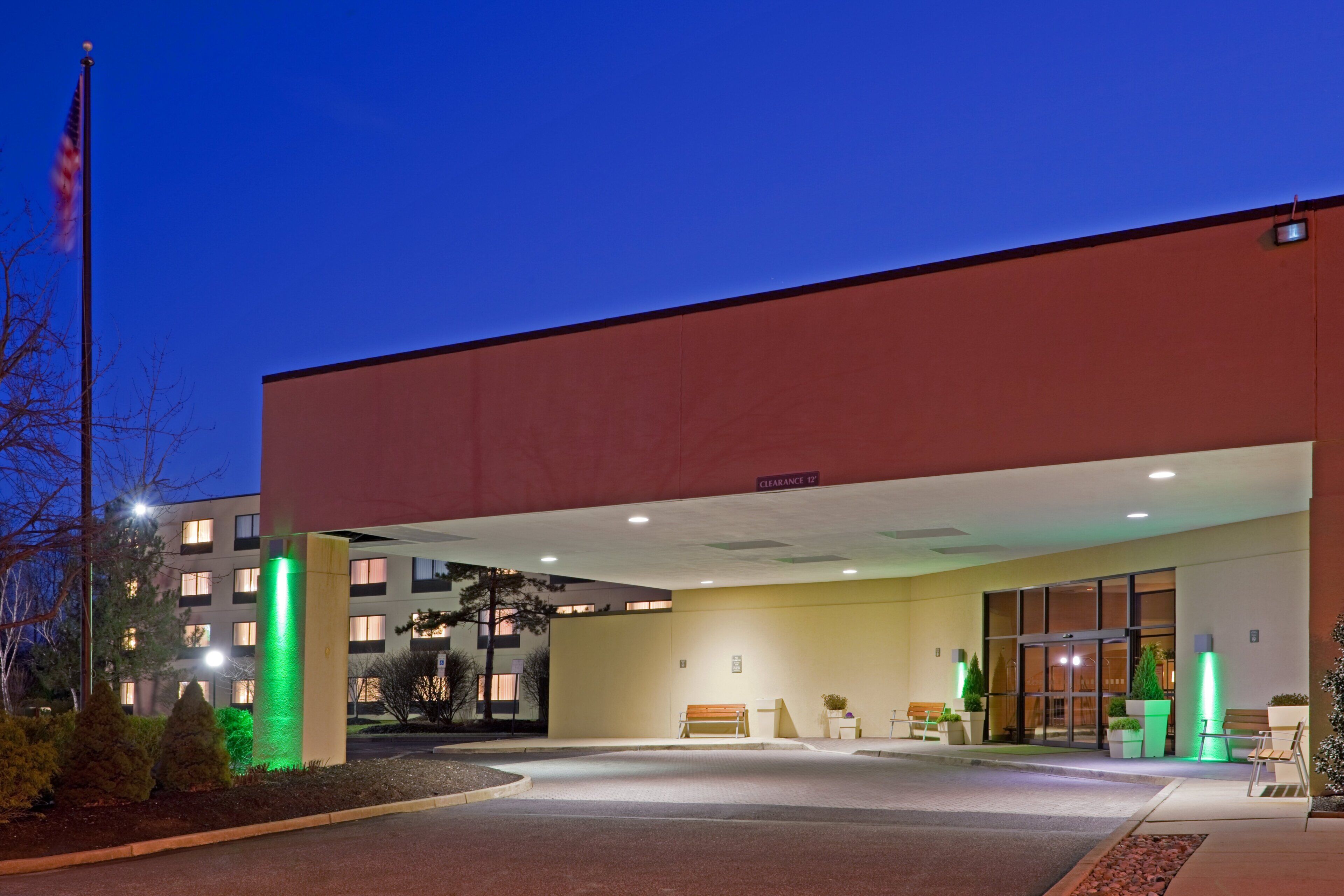 A hotel entrance with a flag, a covered walkway, and a parking area.