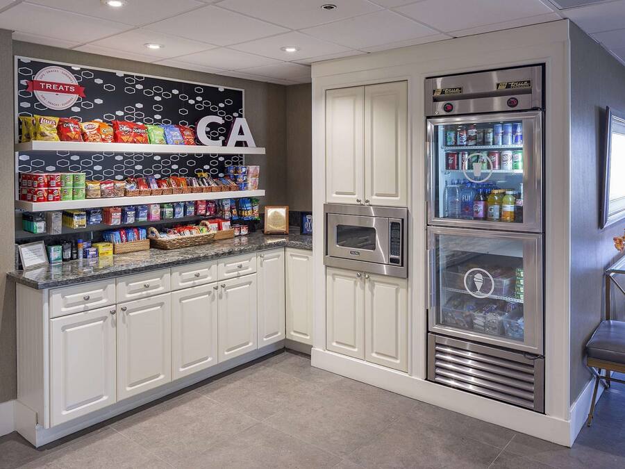 Eine Küche mit weißen Schränken, einer Arbeitsfläche mit Snacks und einem Kühlschrank mit Getränken.