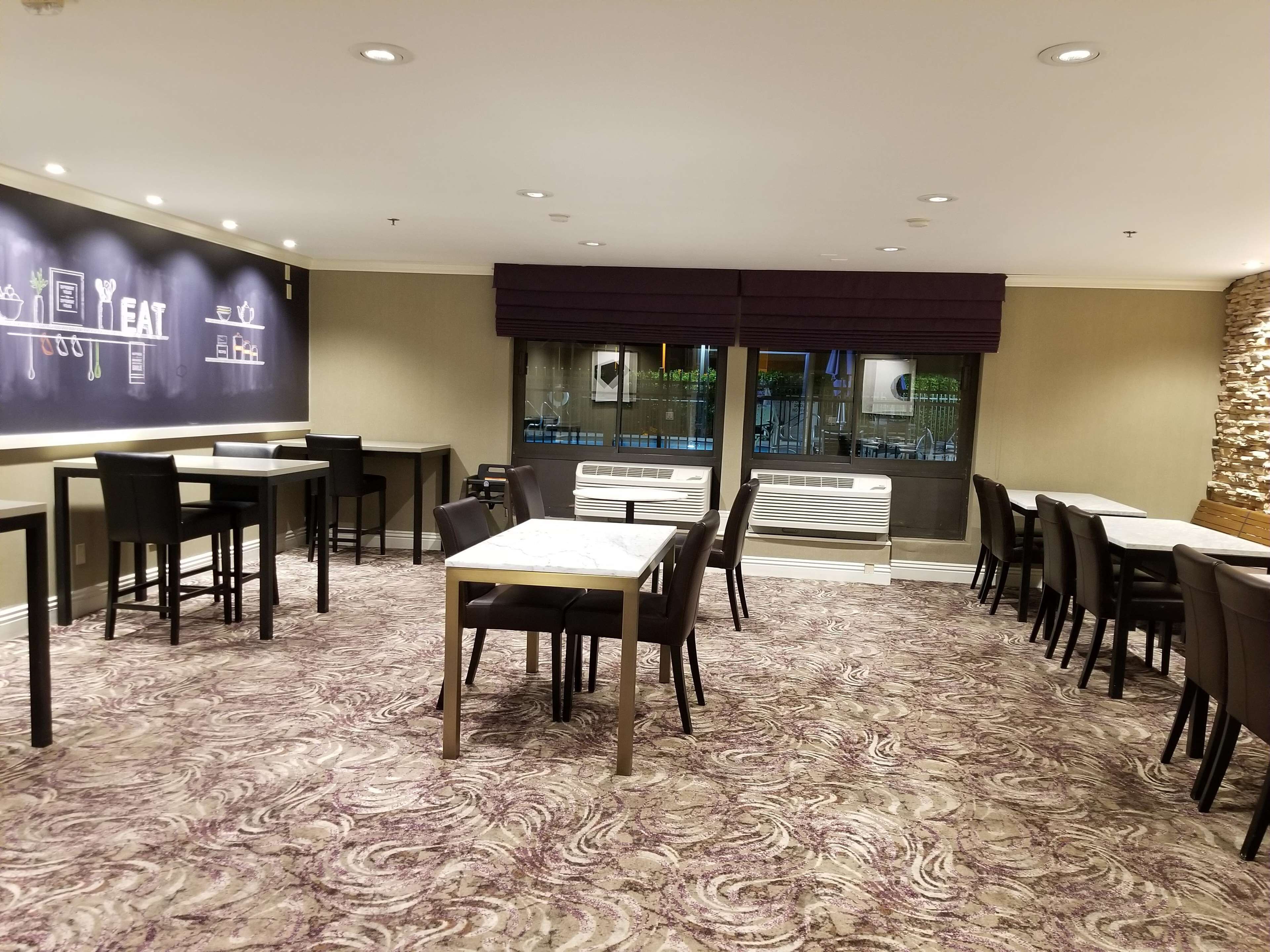 Uma sala de conferências com uma tela de projeção grande, várias mesas e cadeiras, e um carpete estampado.