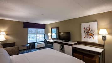 A hotel room with a large bed, a desk, a chair, a TV, and a window with a view.