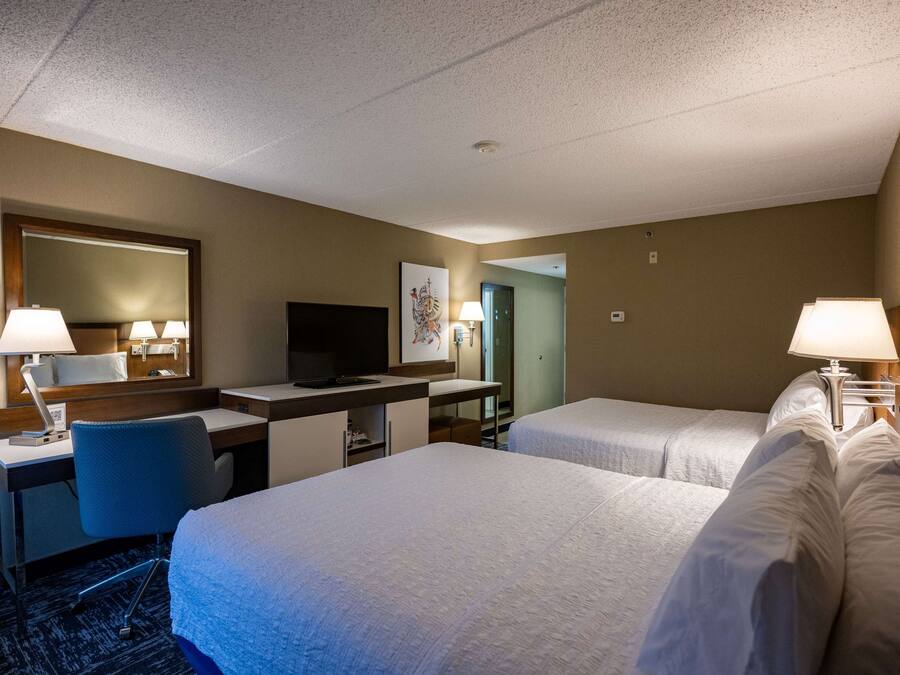 Een hotelkamer met twee bedden, een bureau, een stoel, een televisie en een grote spiegel.