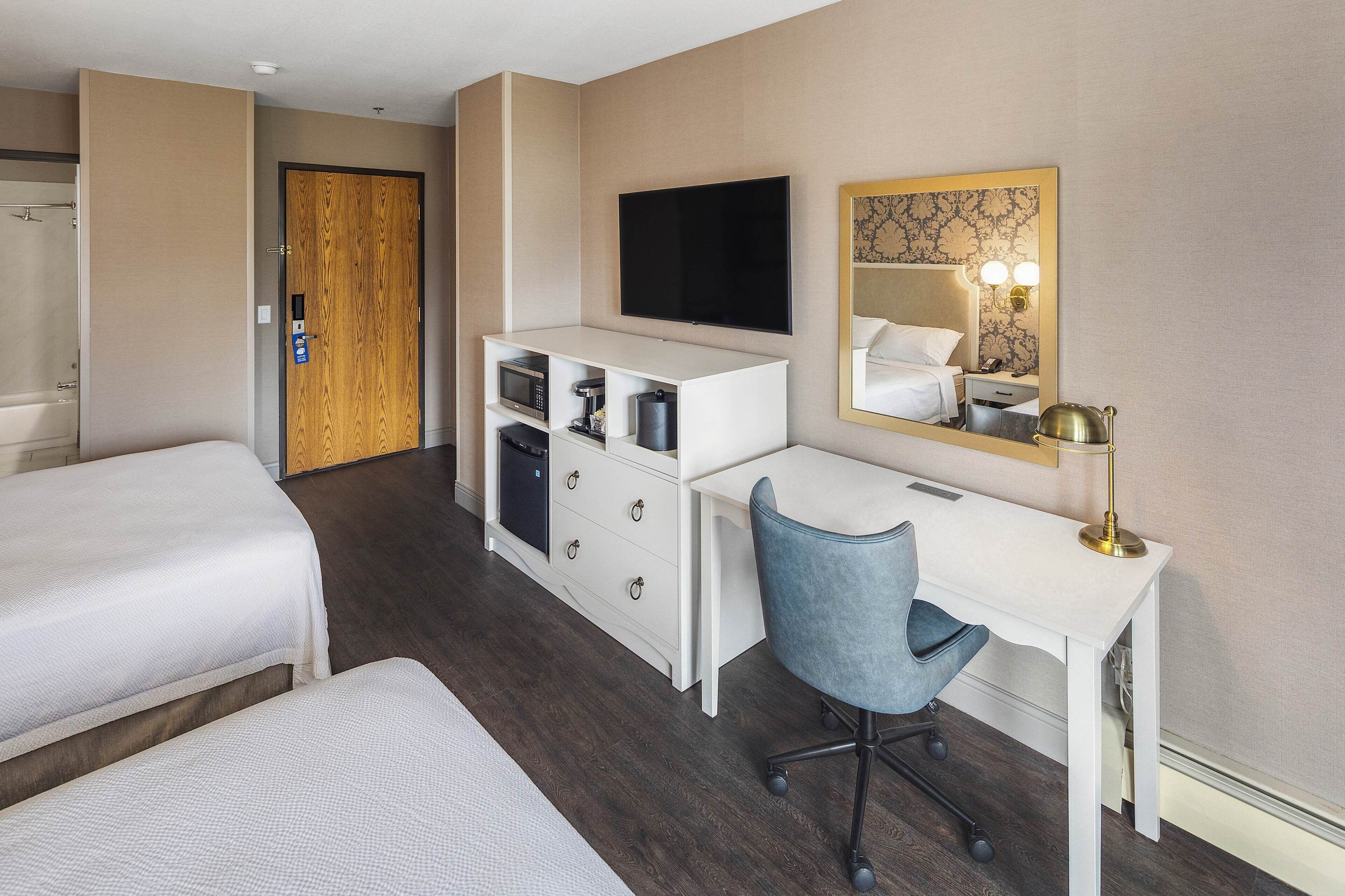 Habitación de hotel con dos camas, un escritorio, una silla, televisión, espejo y un mini bar.