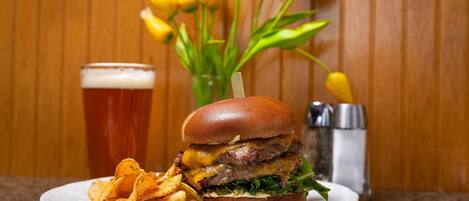 A burger with fries and a glass of beer on a plate, with a bouquet of yellow flowers in the background.