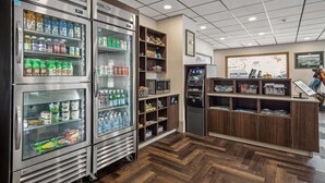 A self-service kiosk area with refrigerated beverage dispensers, a microwave, and a cash register. - Hotel Seward (Seward)