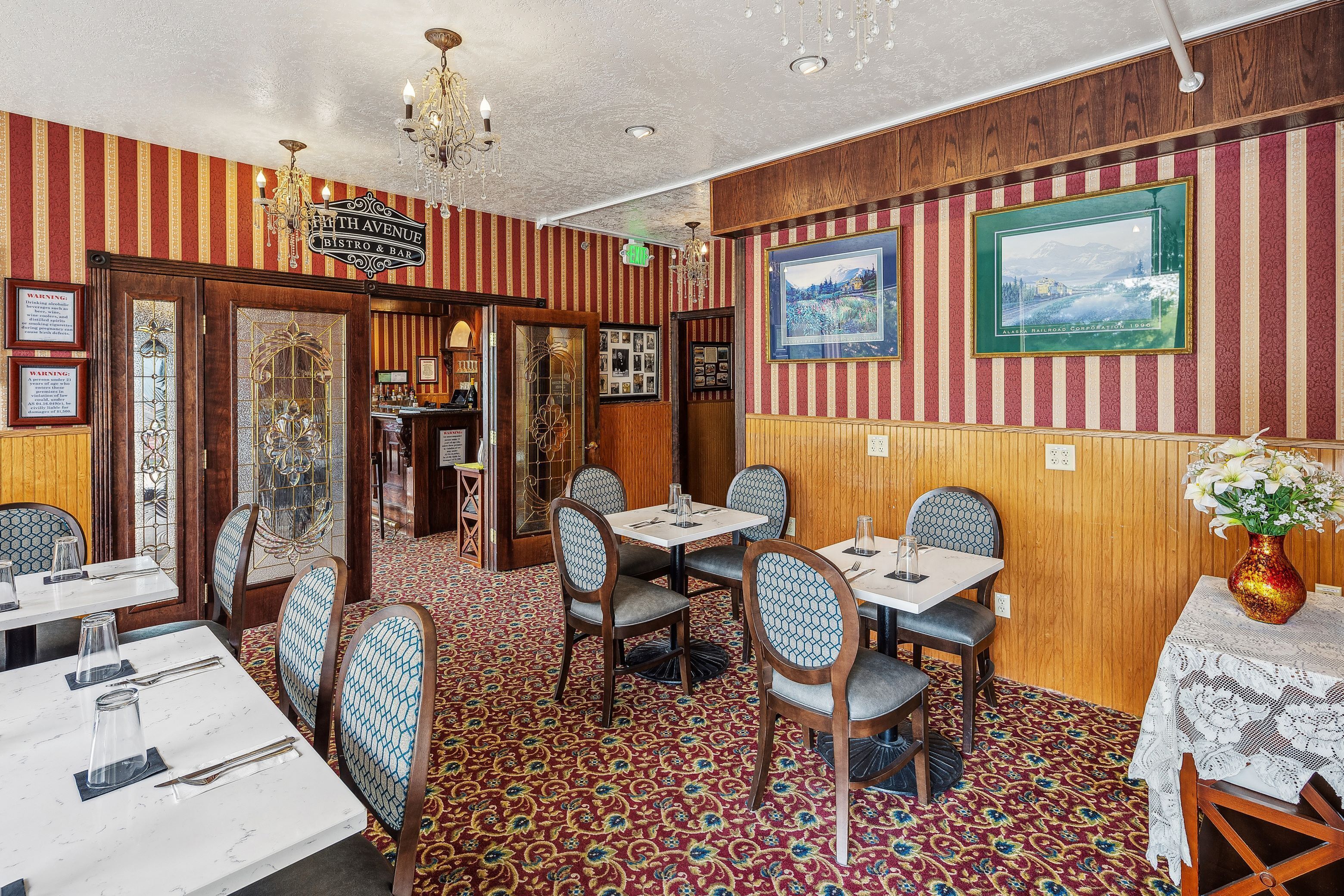 A restaurant interior with striped walls, wooden paneling, and a patterned carpet. Tables and chairs are set for dining.