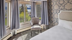 A hotel room with a large bed, a chair, and a view of mountains through the windows. - Hotel Seward (Seward)