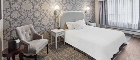 Ein Hotelzimmer mit einem großen Bett, einem Sessel, einem Nachttisch und einer Wanduhr.