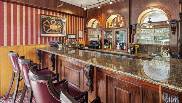 A bar with wooden paneling, striped wallpaper, and bar stools. - Hotel Seward (Seward)