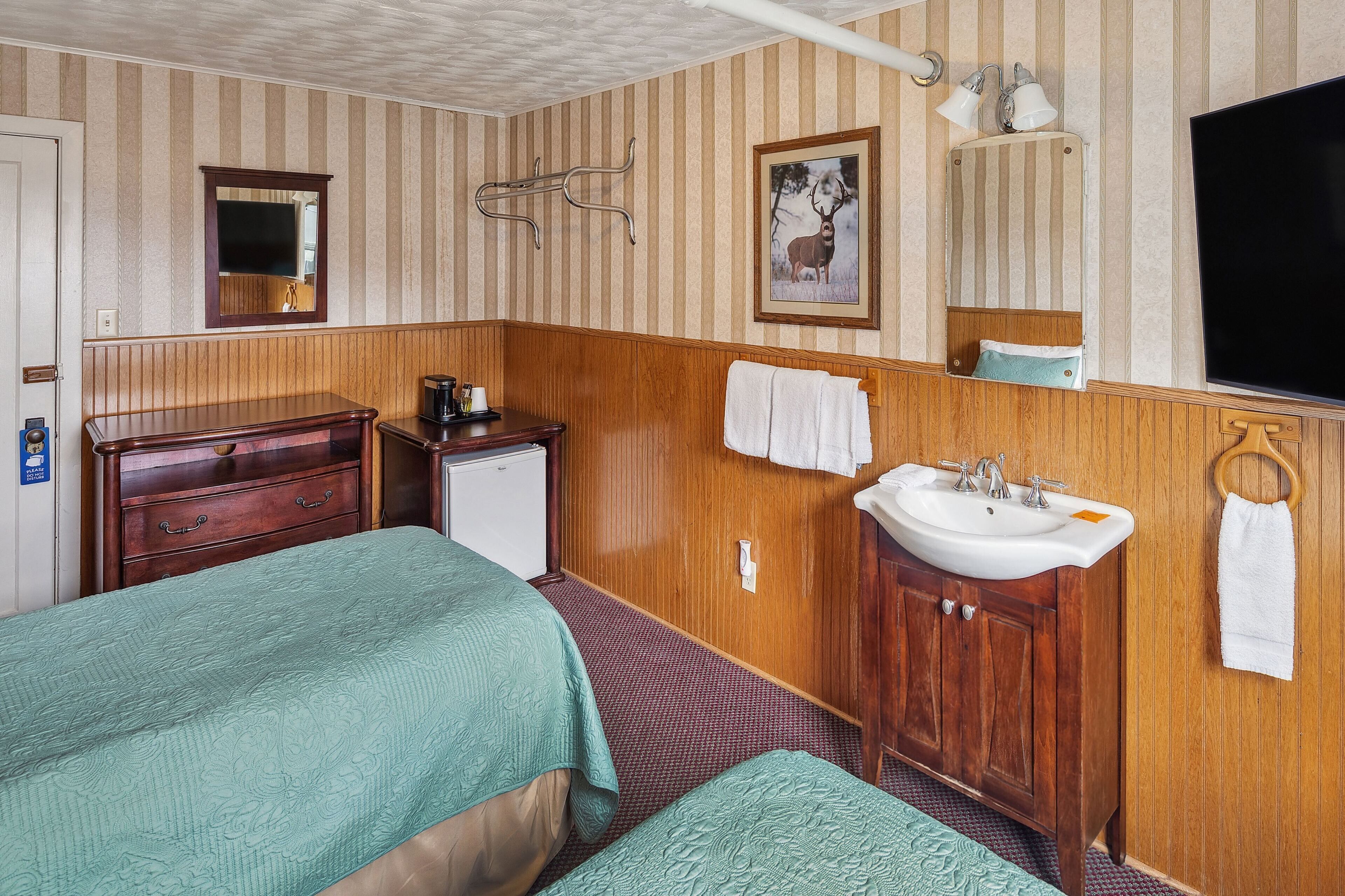 Una habitación de hotel con una cama, un escritorio pequeño con cafetera, un lavabo y un espejo.