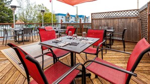 An outdoor patio with tables and chairs, a wooden deck, and a view of buildings in the background. - Hotel Seward (Seward)