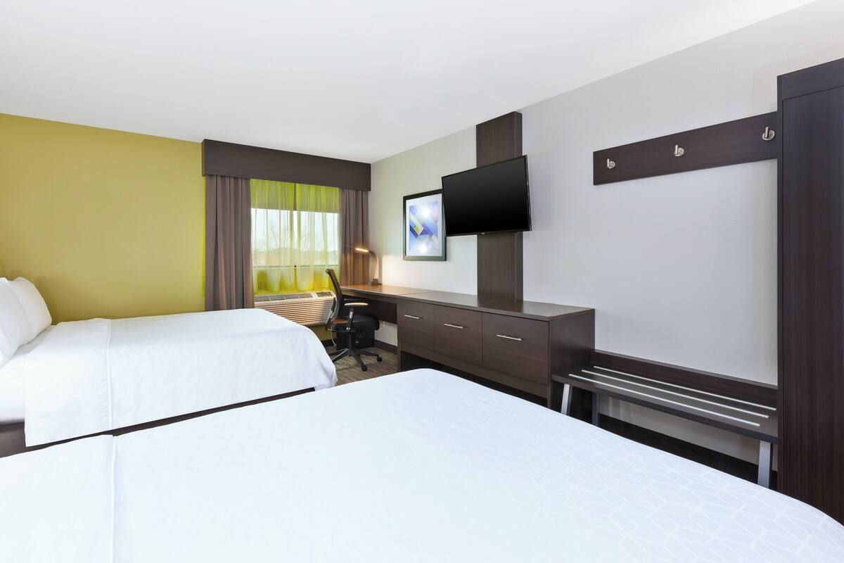 Une chambre d’hôtel avec deux lits, un bureau, une chaise, une télévision et une armoire.