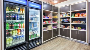 Un espace bien éclairé où l’on peut prendre une collation et boire, avec des boissons réfrigérées et des étagères remplies de collations et de produits emballés.