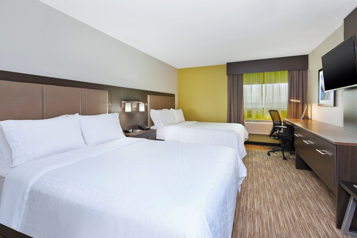 A hotel room with two beds, a desk, a chair, a TV, and a window with curtains.