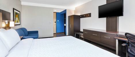 Una habitación de hotel con una cama grande, un escritorio, una silla, un televisor y un armario.