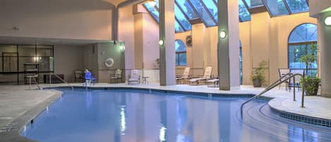 Una piscina interior con techos de vidrio transparente, sillones de descanso y suelo de baldosas.