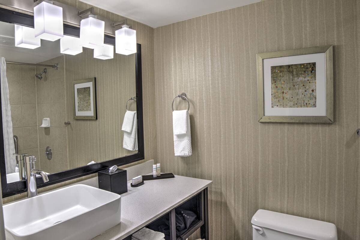 A modern bathroom with a large mirror, two sinks, a toilet, and a framed artwork on the wall.