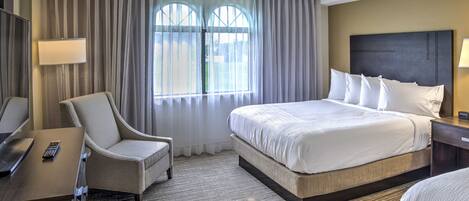 A hotel room with a large bed, a desk with a chair, a lamp, and a view through the window.