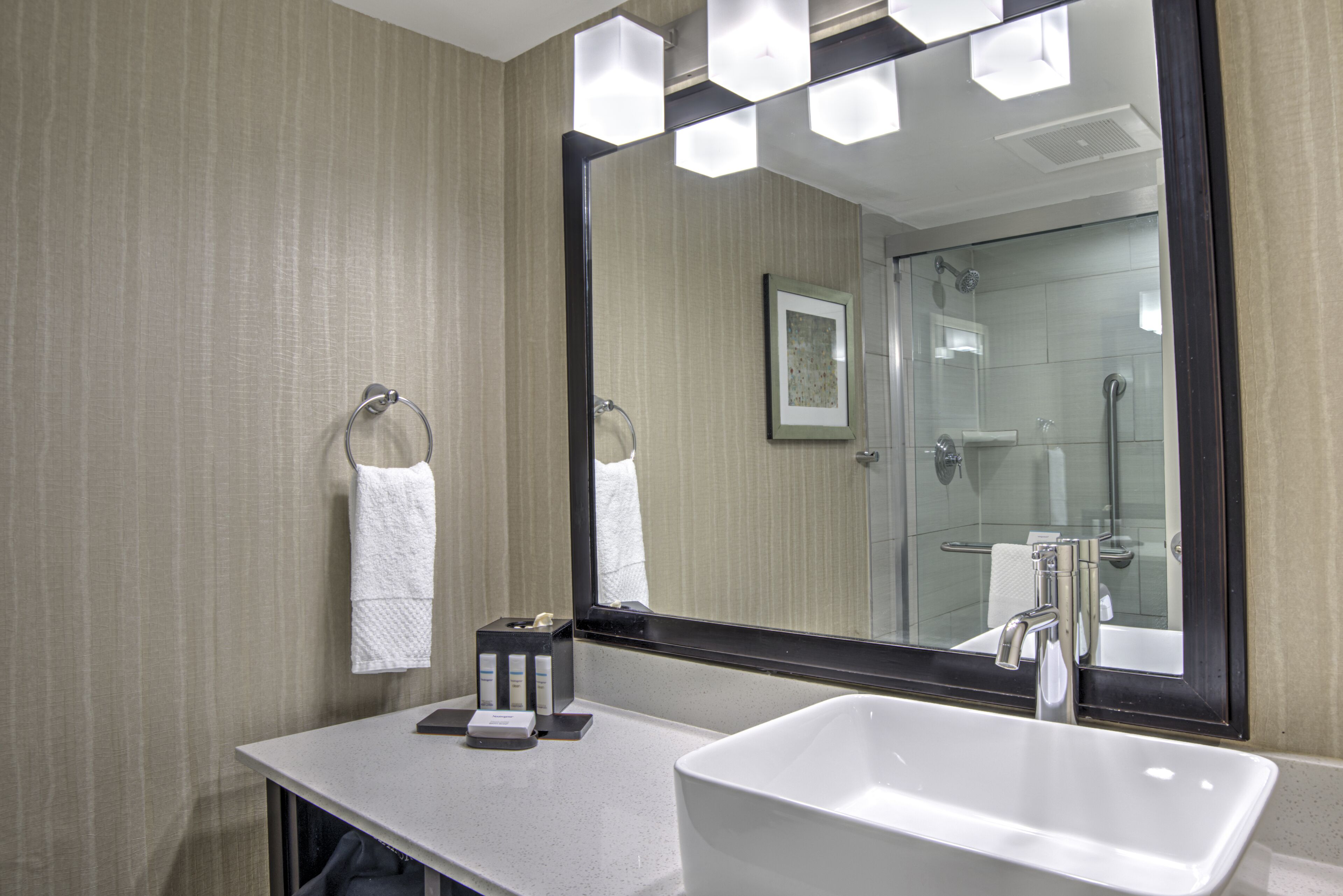 Une salle de bain moderne avec un grand miroir, un lavabo blanc et un porte-serviettes.