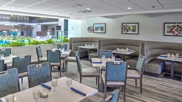 A modern dining area with booths and tables, featuring a view of a pool and greenery outside.
