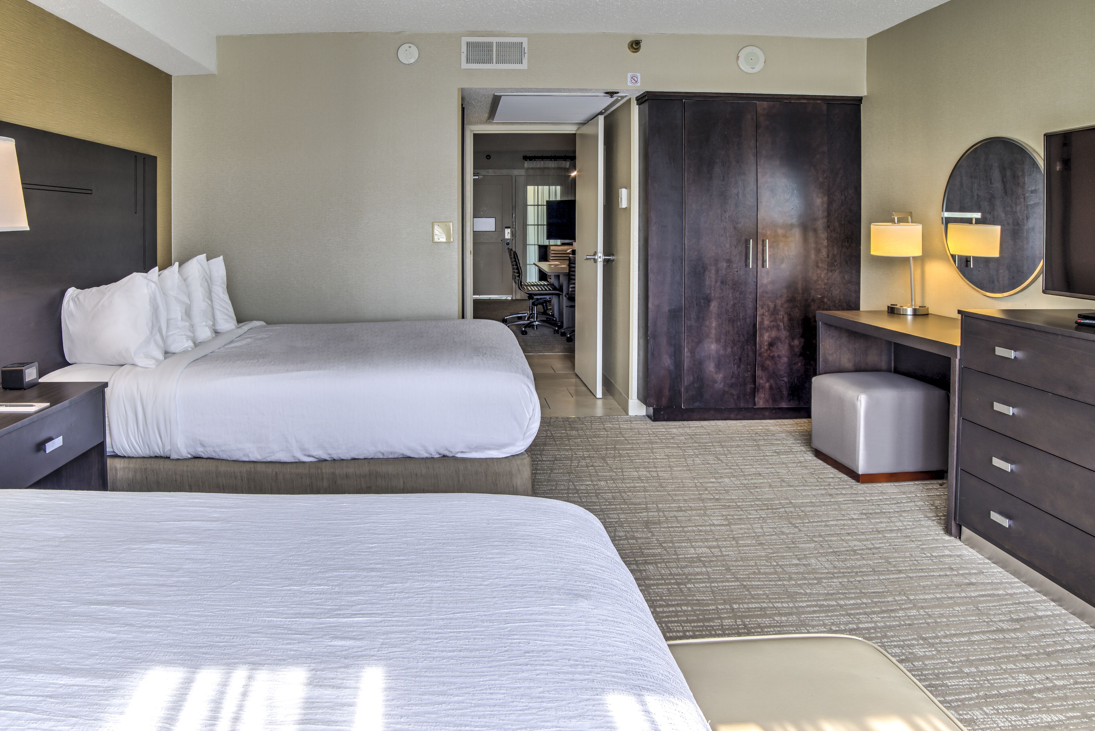 A hotel room with two beds, a desk, a wardrobe, and a bathroom visible through an open door.
