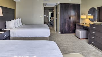 A hotel room with two beds, a desk, a wardrobe, and a bathroom visible through an open door.