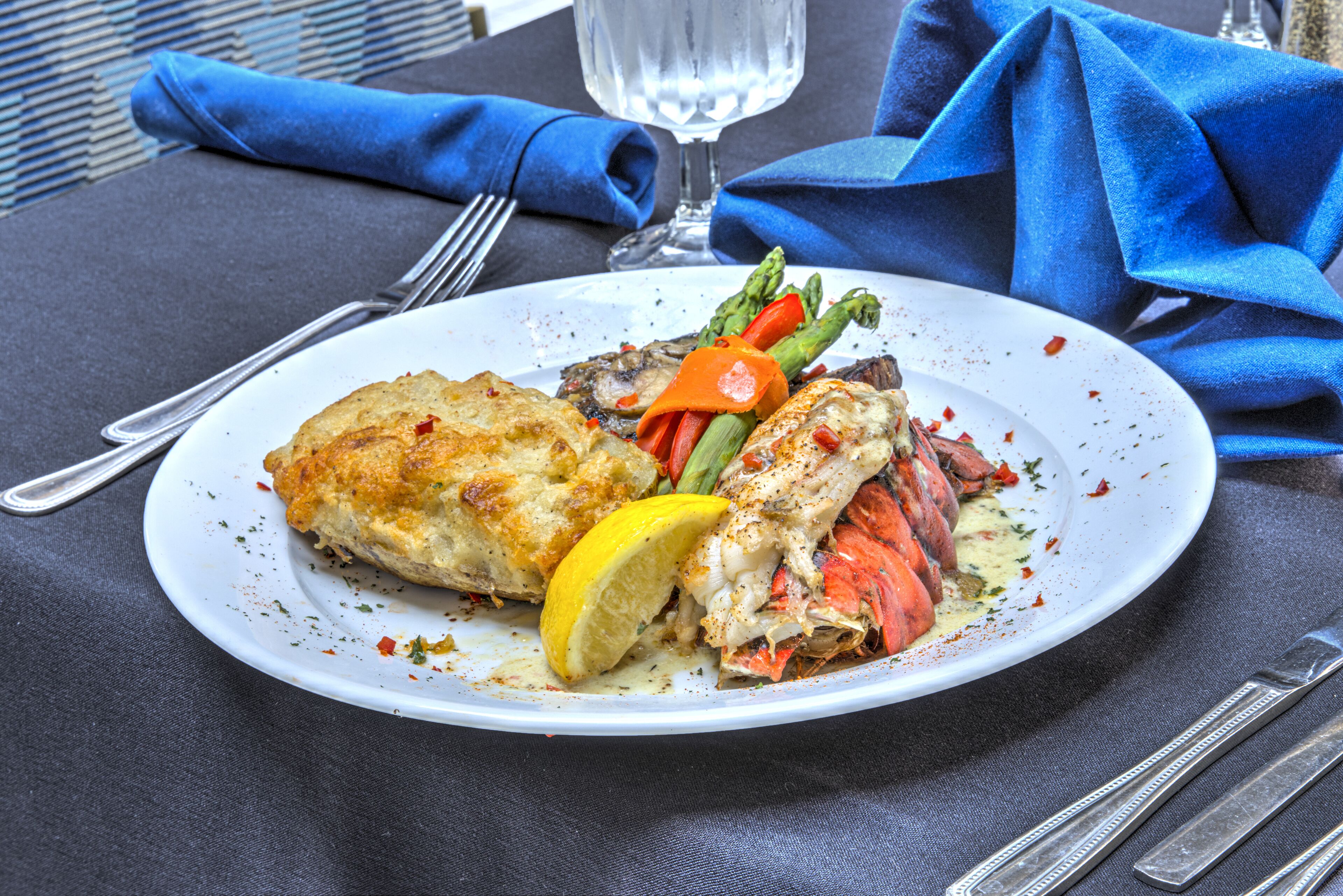 Une assiette de nourriture comprenant une queue de homard, des asperges et une tranche de citron, le tout présenté sur une assiette blanche.