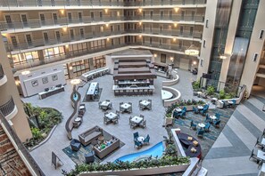 A multi-level hotel atrium with outdoor seating areas, a pool, and multiple floors with balconies.