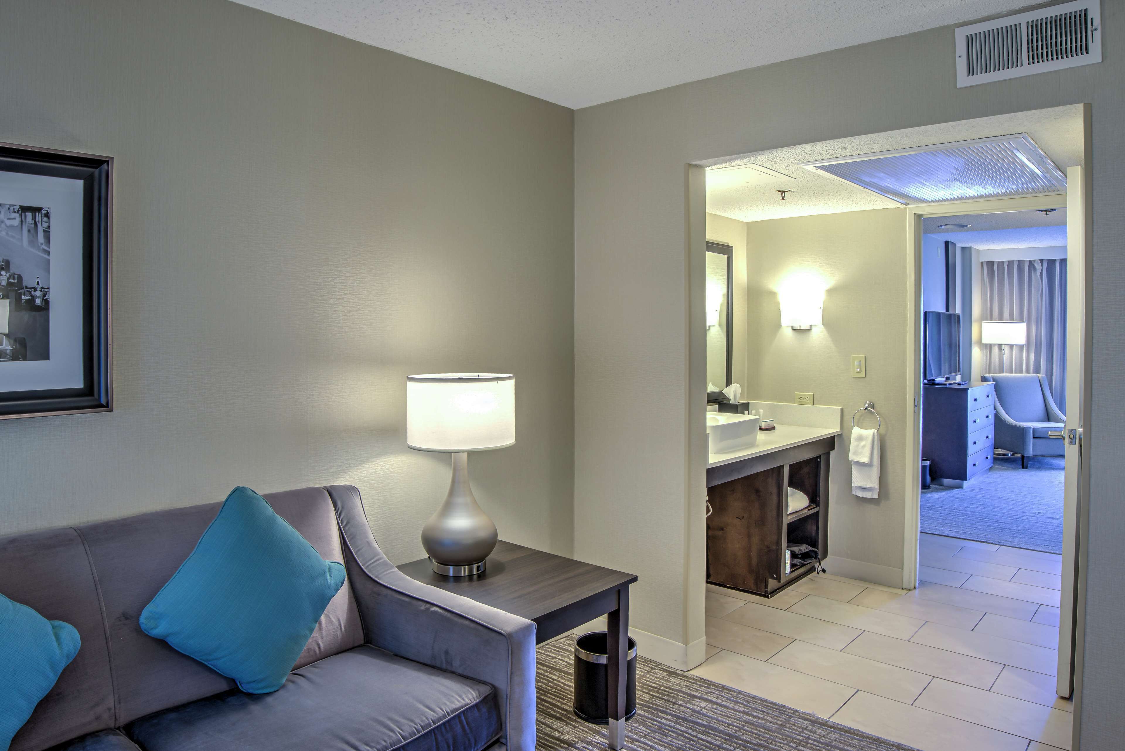 A hotel room with a sofa, a lamp, a framed picture, and a bathroom visible through an open door.