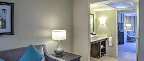 A hotel room with a sofa, a lamp, a framed picture, and a bathroom visible through an open door.