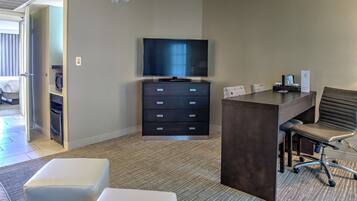 A hotel room with a flat-screen TV, a desk with a chair, a minibar, and a large window.