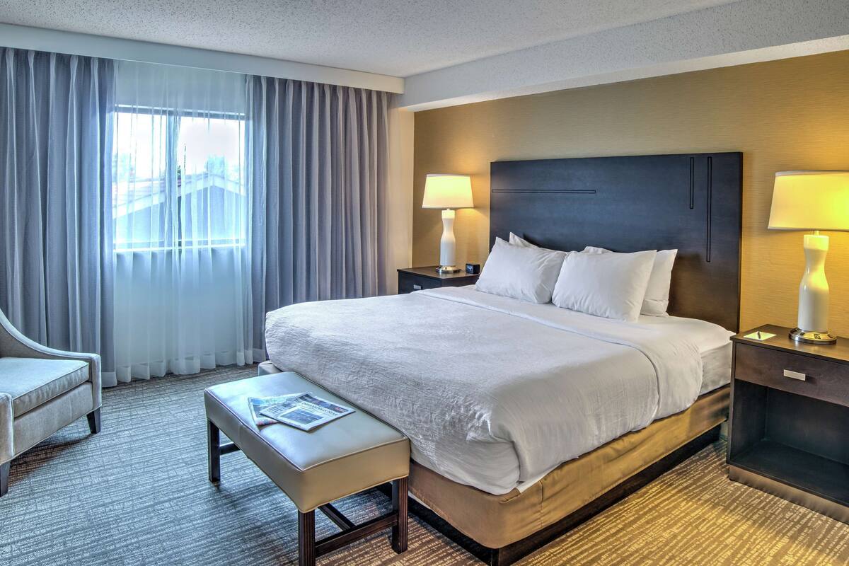 A hotel room with a large bed, a desk, a chair, and a window with curtains.
