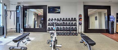 Une salle de sport équipée de matériel d’exercice, notamment des tapis de course, un vélo d’appartement et un banc de musculation. On y trouve également des rangées d’haltères et un distributeur d’eau.