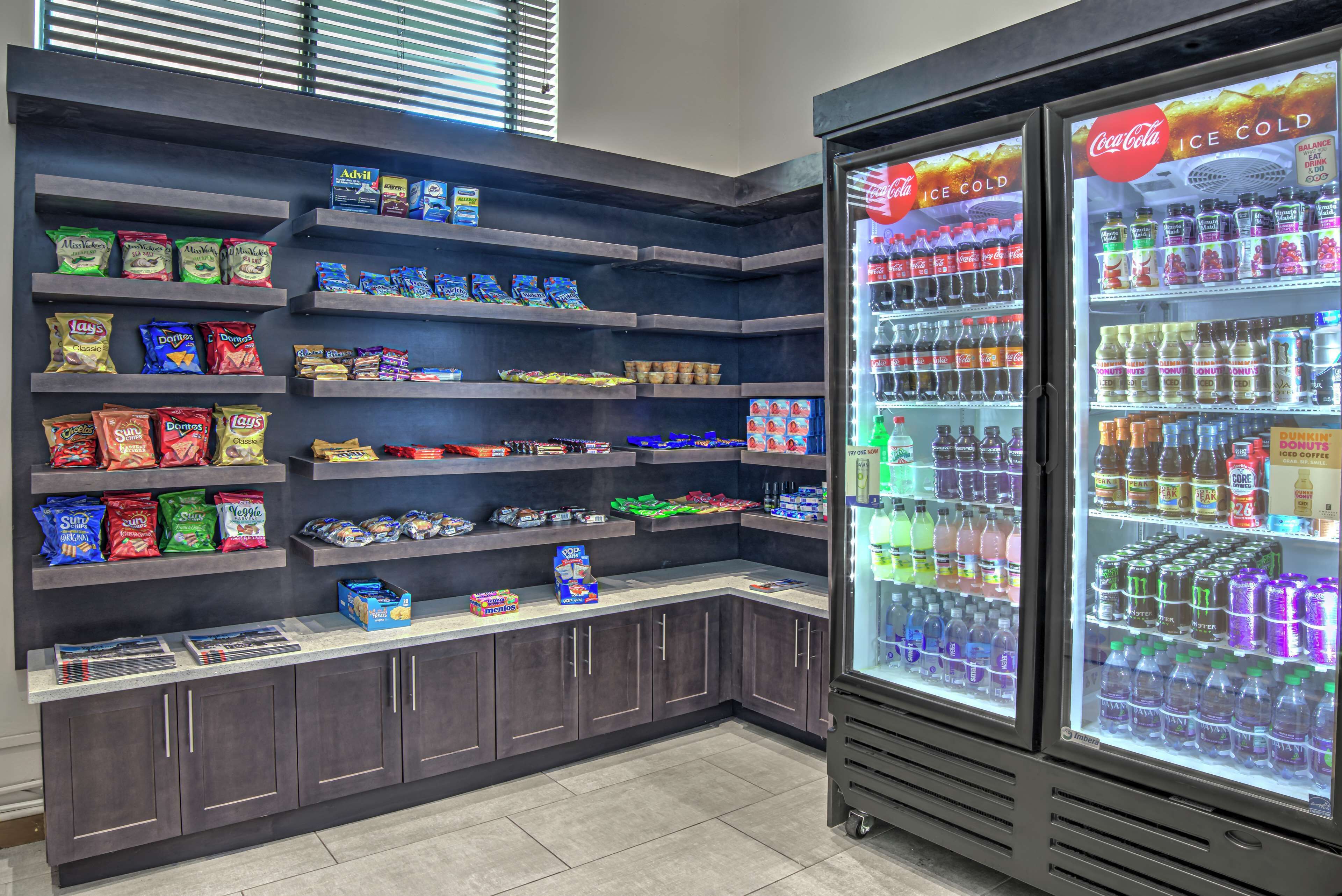 A snack and beverage vending area with shelves stocked with various snacks and a Coca-Cola refrigerator.