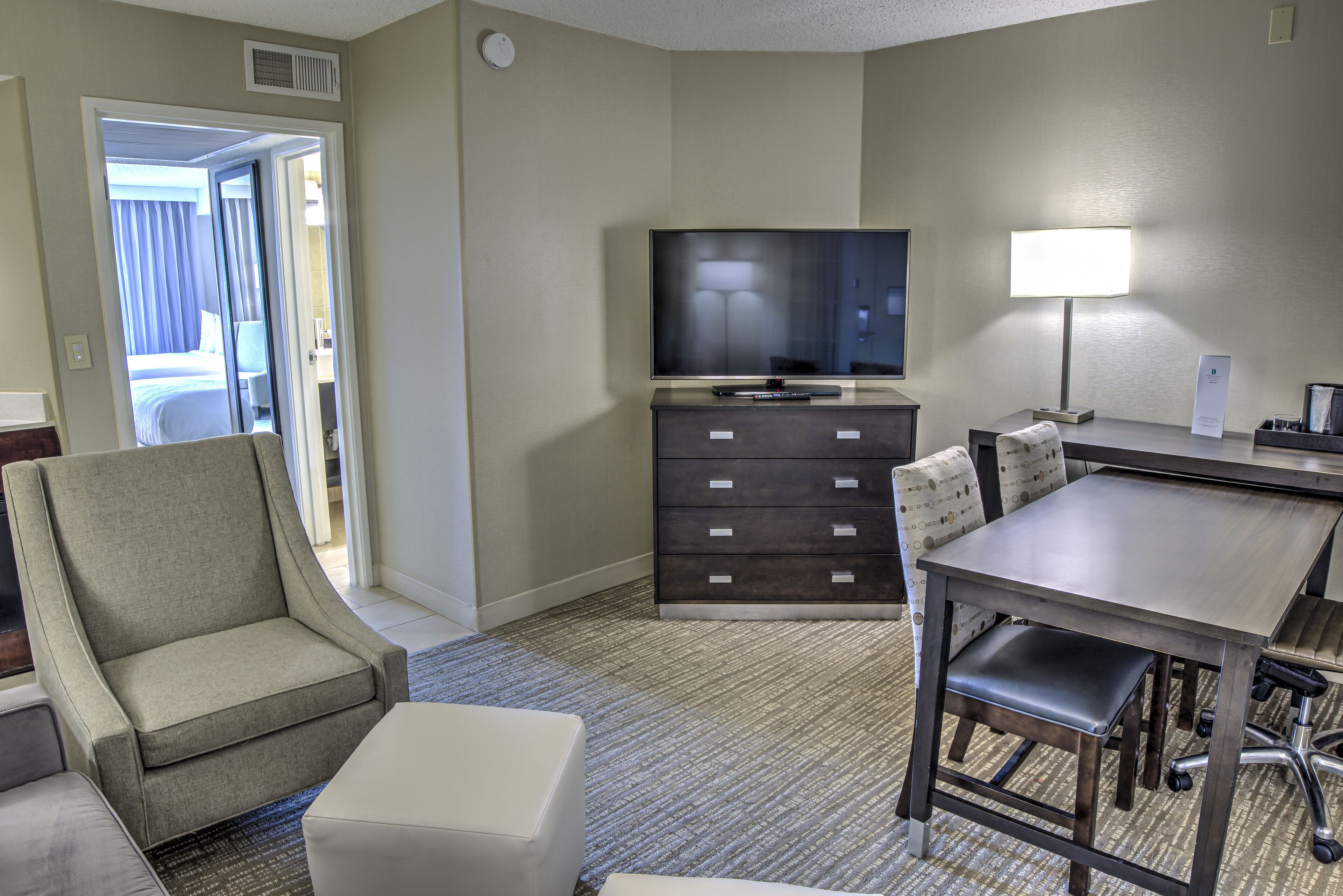 Une chambre d’hôtel équipée d’une télévision à écran plat, d’un bureau avec une lampe, d’une chaise, d’un canapé et d’une petite table.