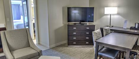 Une chambre d’hôtel équipée d’une télévision à écran plat, d’un bureau avec une lampe, d’une chaise, d’un canapé et d’une petite table.