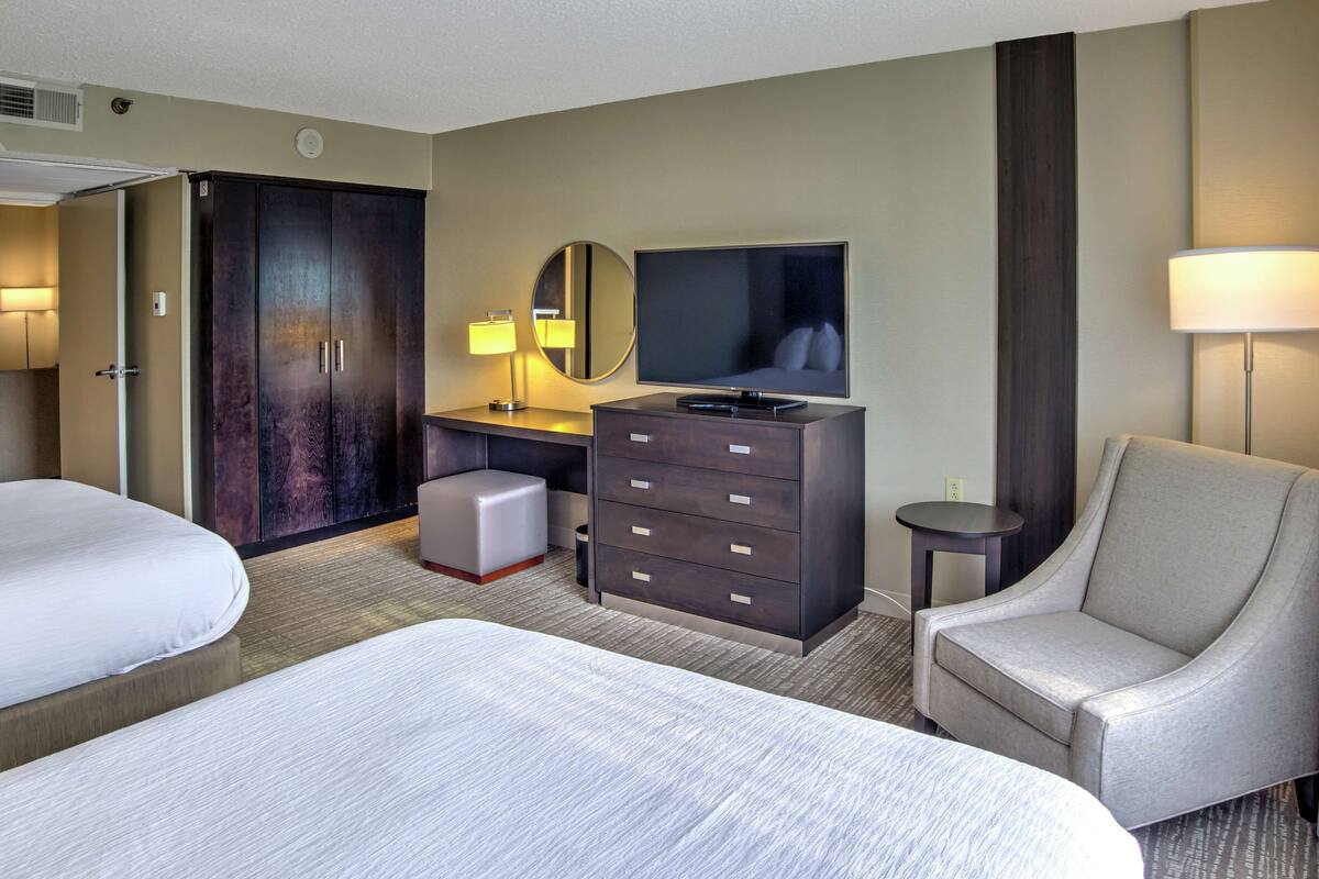 A hotel room with two beds, a desk with a TV, a chair, a wardrobe, and a mirror.