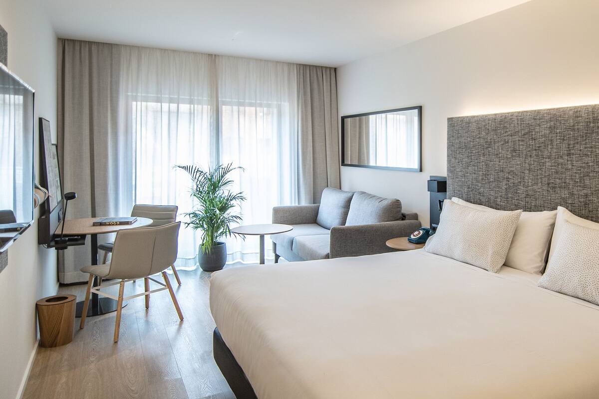 Una habitación de hotel moderna con una cama grande, un sofá, una mesa de comedor y un televisor.