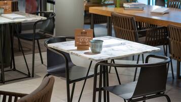 Ein modernes Café mit Tischen, Stühlen, großen Fenstern und einer Pflanze in der Mitte.