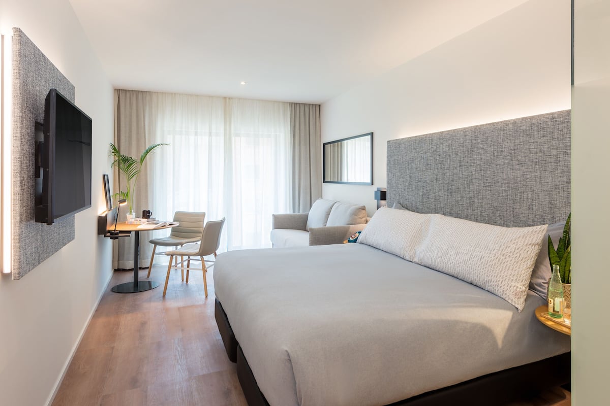 Una habitación de hotel moderna con una cama grande, un escritorio con una silla, un sofá y un televisor montado en la pared.