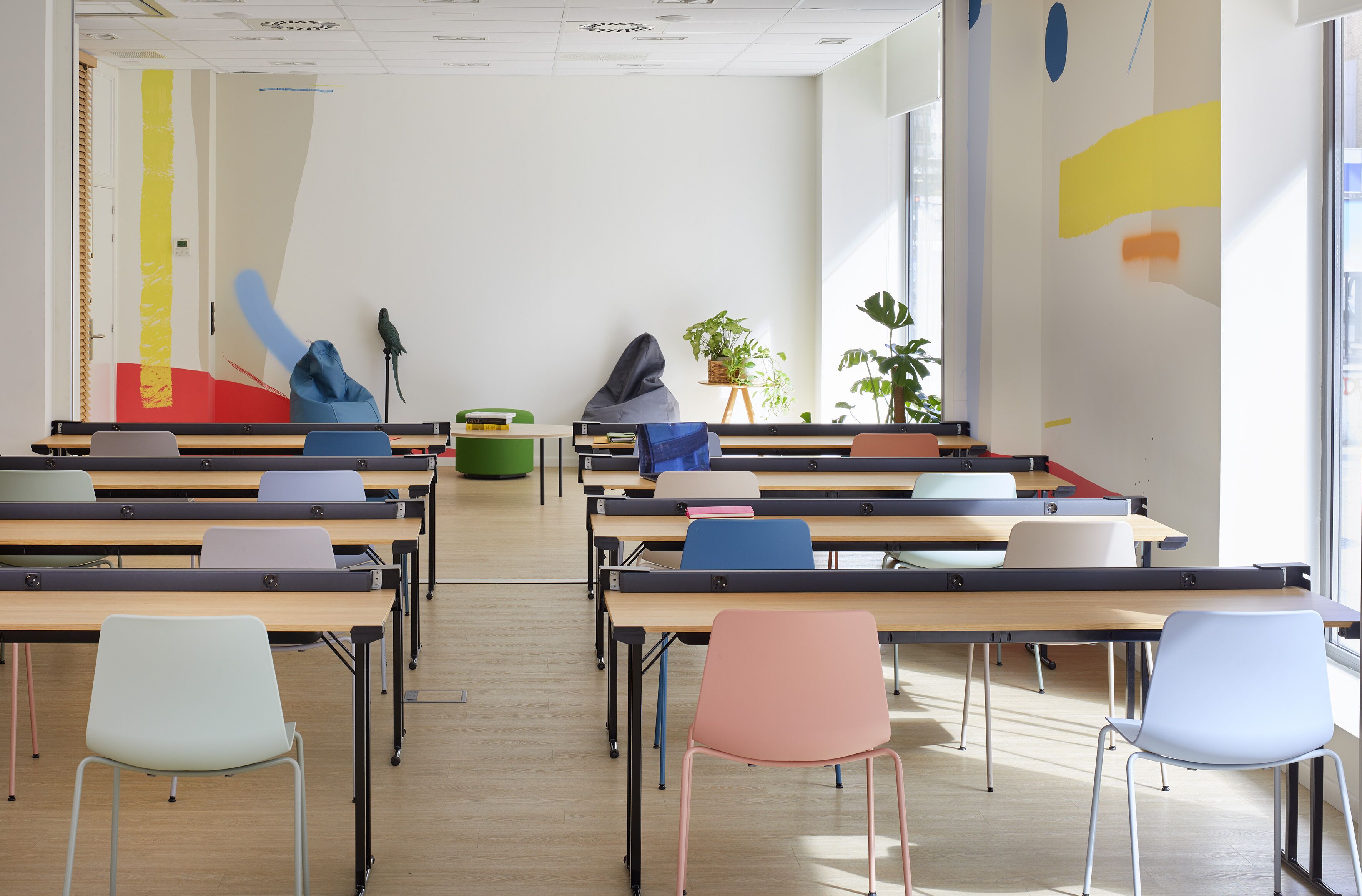 Un aula con filas de escritorios y sillas, una planta verde y un pájaro en un atril.