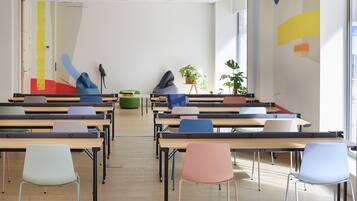 Un aula con filas de escritorios y sillas, una planta verde y un pájaro en un atril.