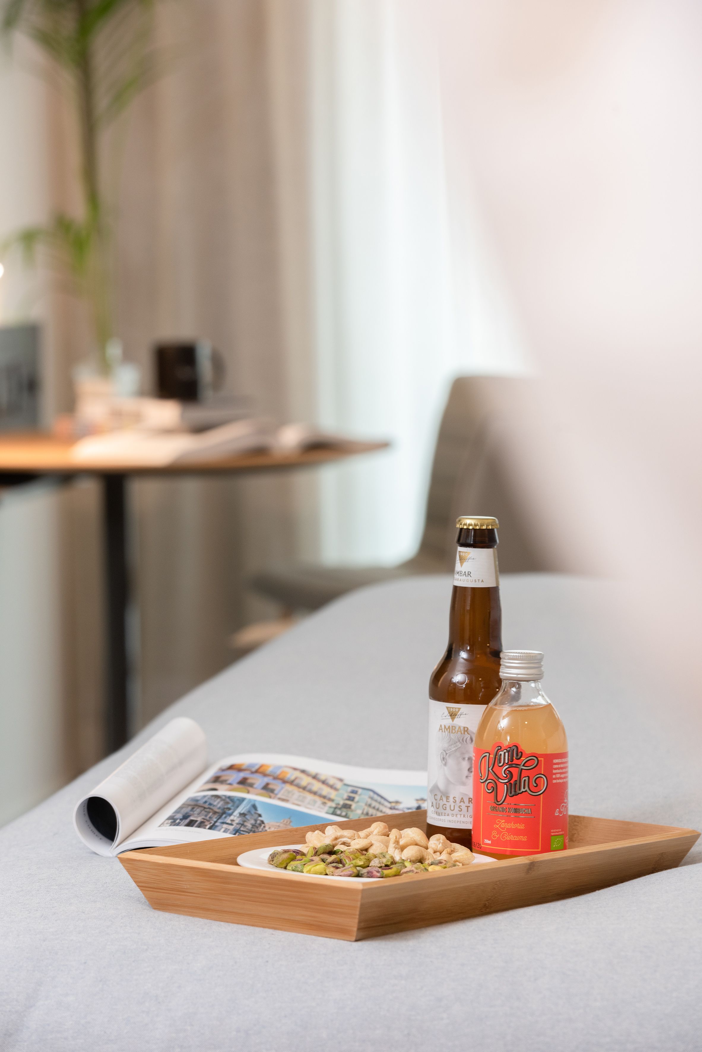 Ett bricka med en ölflaska, en vinflaska och en juiceflaska står på ett bord tillsammans med en tidning och lite mat.