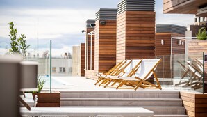 Una terraza en la azotea con sillones de madera, una piscina y arquitectura moderna.
