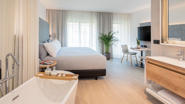 Una habitación de hotel moderna con una cama grande, un baño con bañera, un escritorio con silla y una televisión.