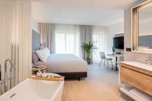 A modern hotel room with a large bed, a bathroom with a bathtub, a desk with a chair, and a television. - INNSiDE by Meliá Zaragoza (Zaragoza)